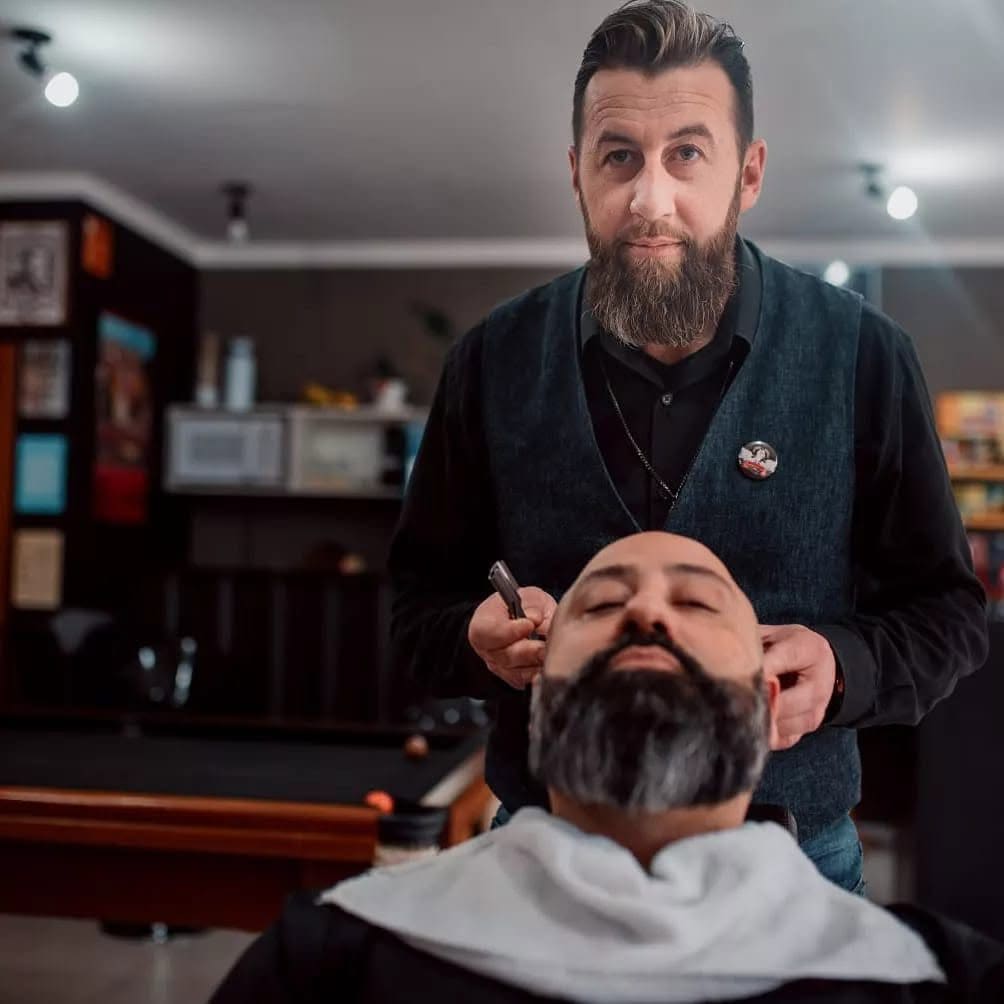 Barbeiro fazendo o contorno da barba de um cliente na cadeira